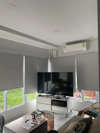 Modern living room with sleek furniture and large TV, featuring natural light from windows.