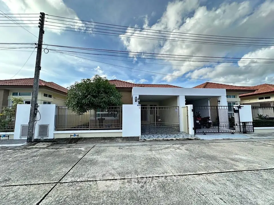 Charming single-story house with gated driveway and lush greenery under a bright blue sky.