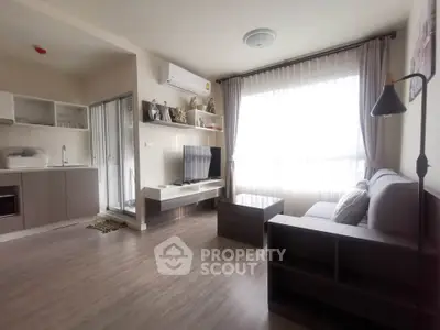 Modern living room with open kitchen, featuring sleek furniture and large window for natural light.