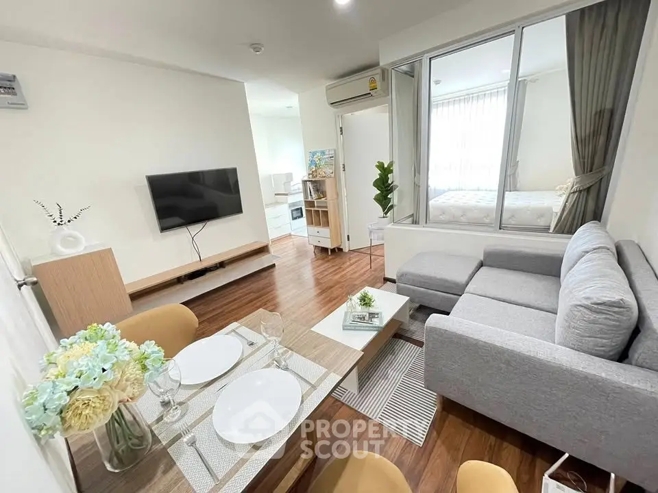 Modern living room with cozy gray sofa, wall-mounted TV, and elegant dining setup in bright apartment.