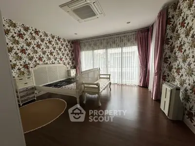 Charming bedroom with floral wallpaper and elegant furniture, featuring large windows and wooden flooring.