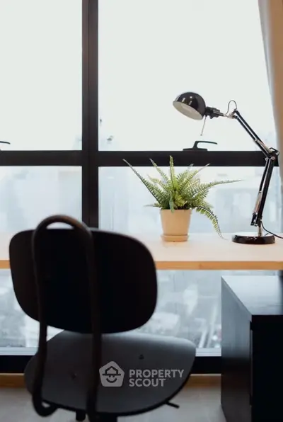 Modern study area with desk lamp and potted plant by large window.
