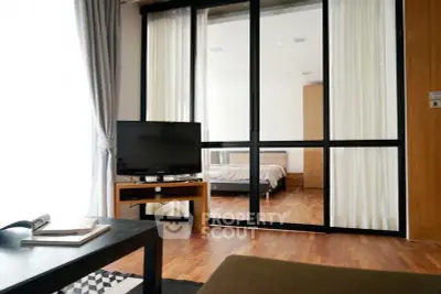 Modern living room with sliding glass doors leading to a cozy bedroom, featuring wooden flooring and stylish decor.