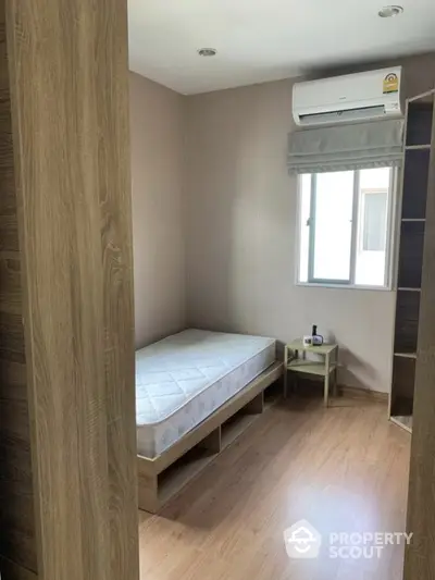 Cozy bedroom with ample natural light, featuring a comfortable bed, air conditioning unit, and sleek wooden flooring, ideal for restful living.