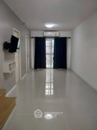 Spacious living room with glossy tiled floors and mounted TV, featuring large window for natural light.