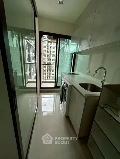 Modern compact kitchen with washing machine and balcony view in high-rise apartment.