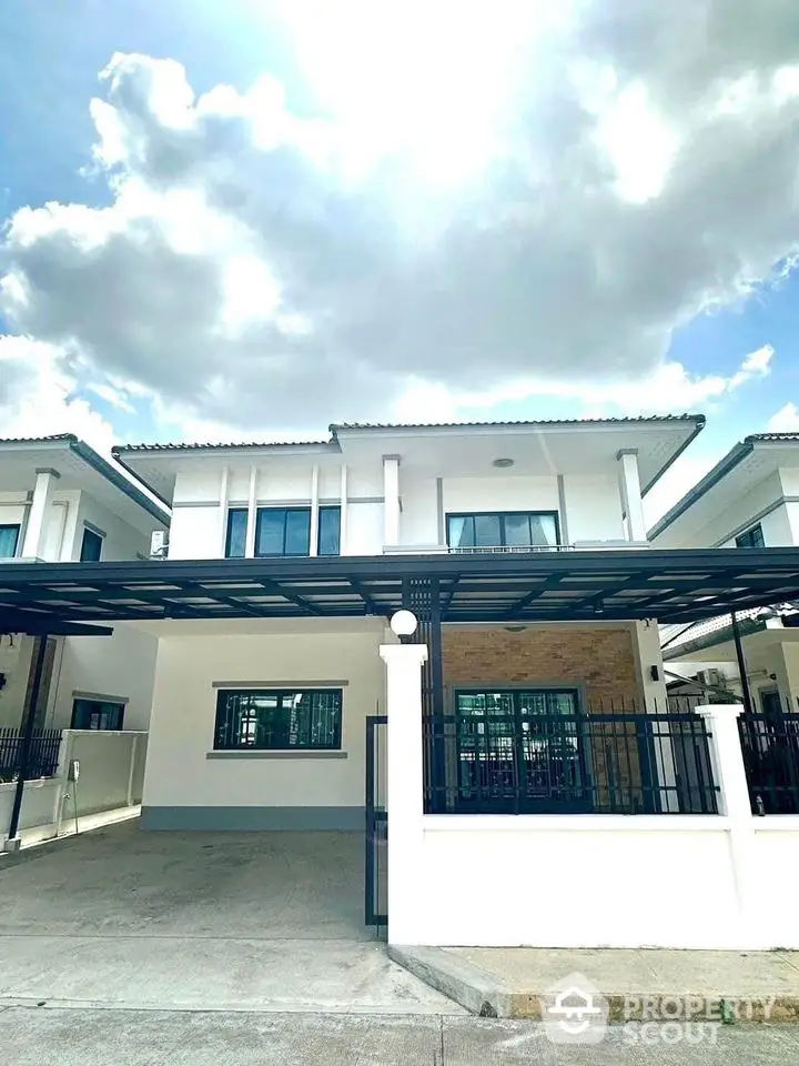 Modern two-story house with spacious carport and elegant facade under a bright sky.