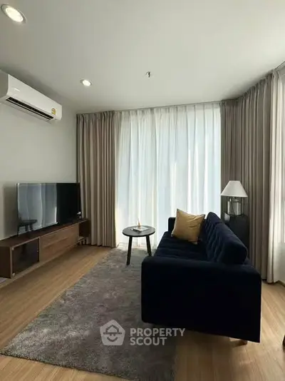 Modern living room with stylish furniture and natural light, featuring a sleek TV setup and elegant curtains.