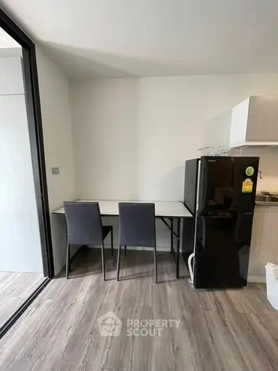Modern kitchen with sleek black fridge and dining area in stylish apartment.