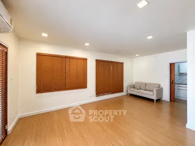 Spacious living room with wooden flooring and modern sofa, featuring large windows with blinds.