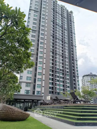 Modern high-rise apartment building with lush green landscaping and outdoor seating area.