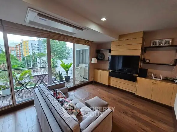 Modern living room with large windows and balcony view, featuring stylish furniture and wooden flooring.