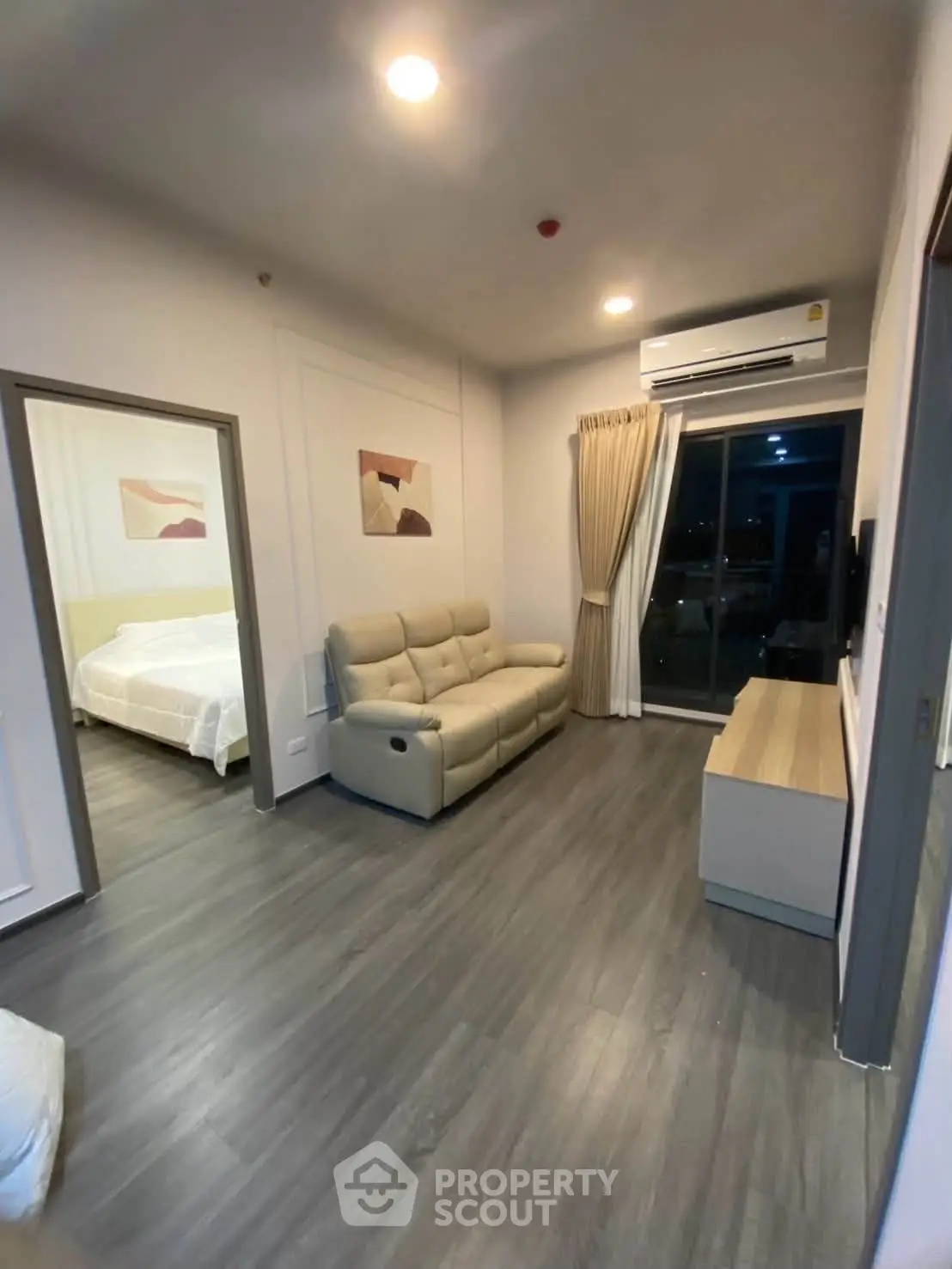 Modern living room with sleek flooring, cozy sofa, and air conditioning, leading to a stylish bedroom.