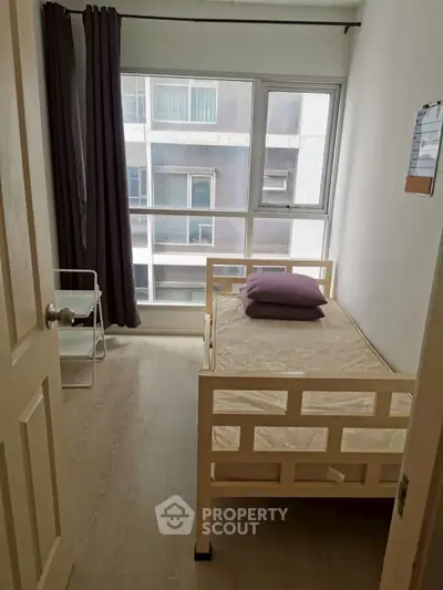 Cozy bedroom with single bed and large window offering natural light in modern apartment.