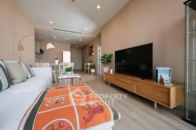 Modern living room with stylish decor and large TV, open layout to dining area.