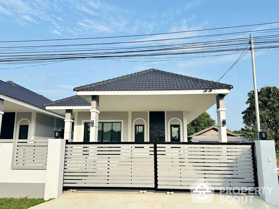 Modern single-story house with sleek design and gated entrance under clear blue sky.