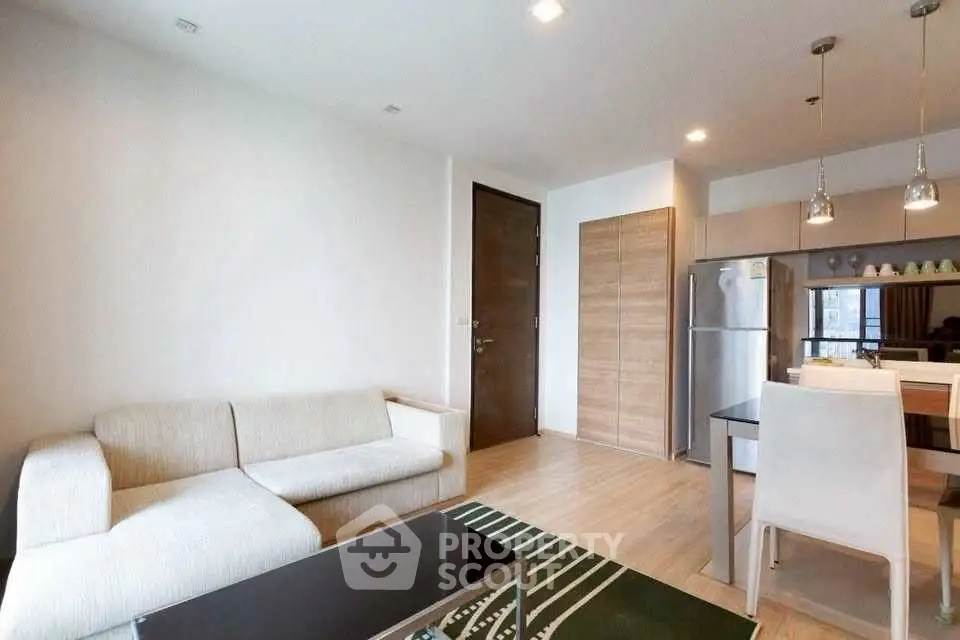 Modern living room with open kitchen, featuring sleek furniture and contemporary lighting.