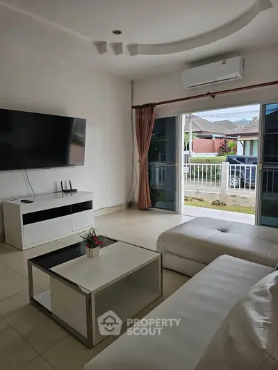 Modern living room with sleek furniture and large TV, featuring a view of the outdoor area through sliding glass doors.