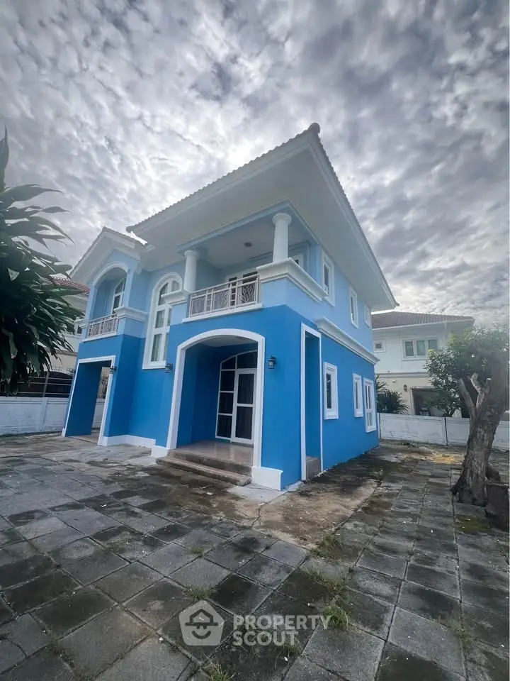 Stunning blue two-story house with elegant columns and spacious driveway under a dramatic cloudy sky.