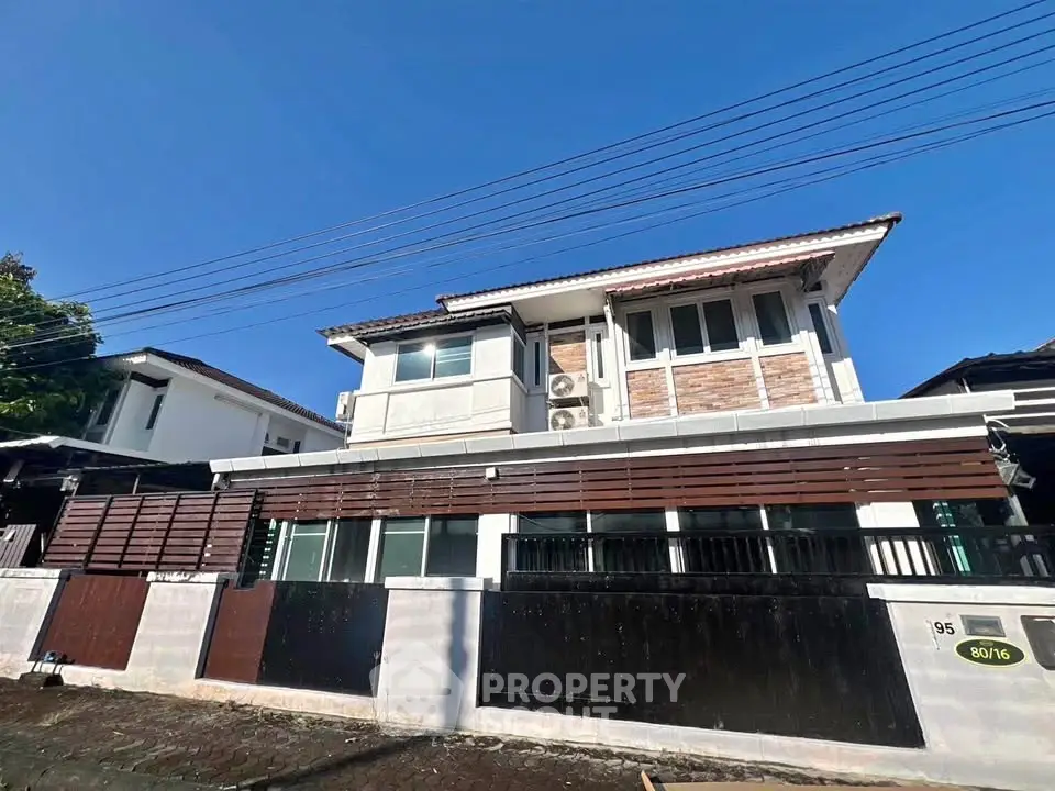Modern two-story house with stylish facade and gated entrance in a suburban neighborhood.