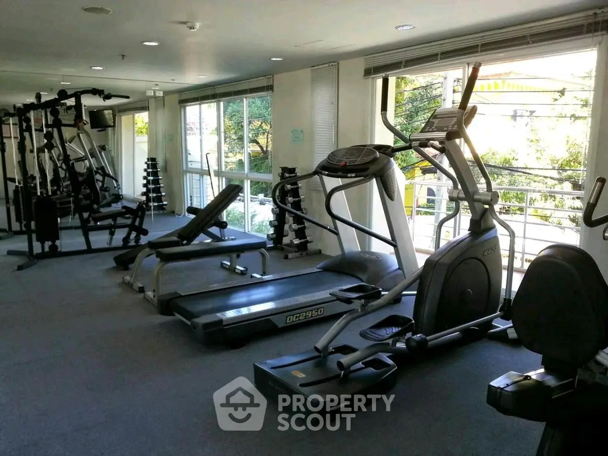 Spacious gym with modern equipment and large windows offering natural light.