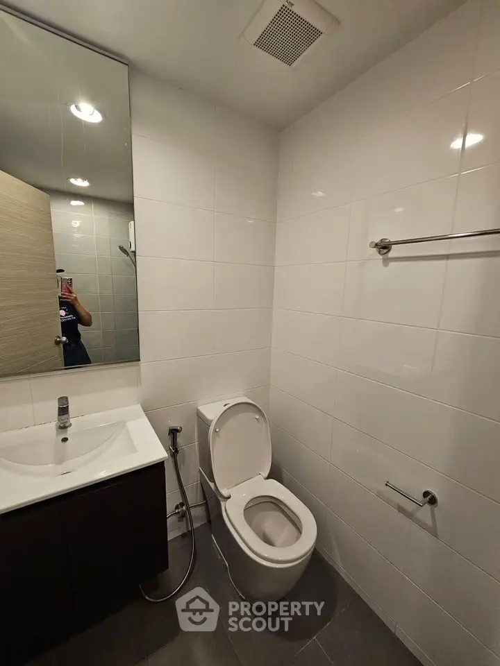 Modern bathroom with sleek fixtures and white tiled walls, featuring a toilet and vanity sink.