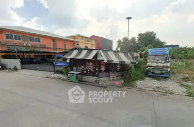 Street view of small roadside shop with striped awning and colorful building in background.
