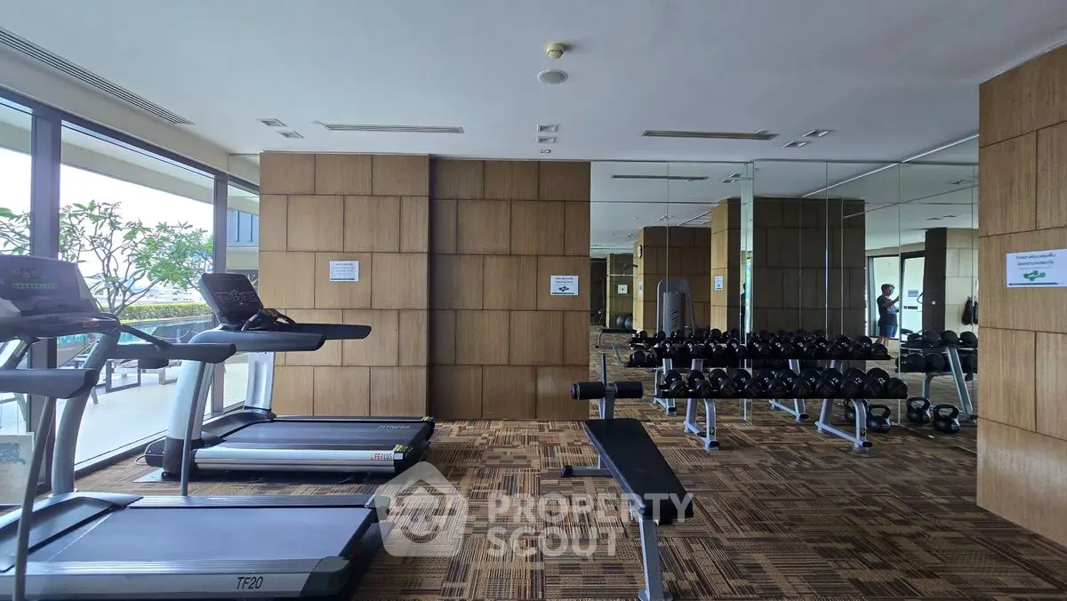 Spacious gym with modern equipment and mirrored walls in luxury apartment complex.