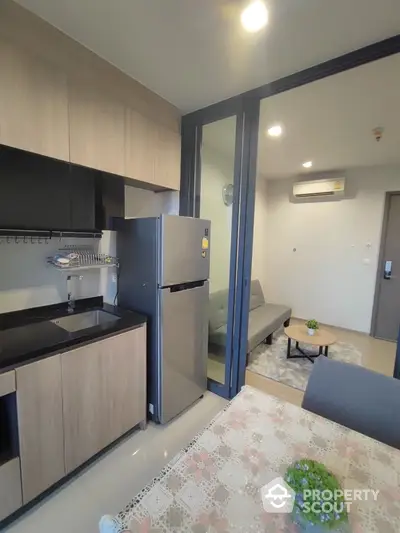 Modern compact kitchen with sleek appliances and cozy living area in open layout apartment.