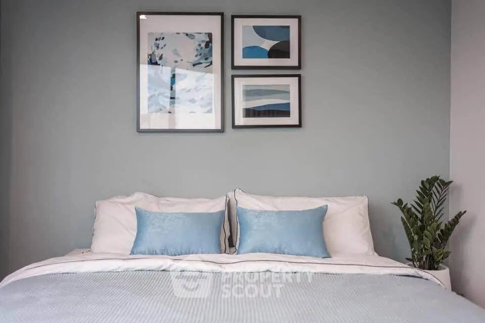 Stylish bedroom with modern decor and cozy bedding, featuring framed art and a potted plant for a serene ambiance.