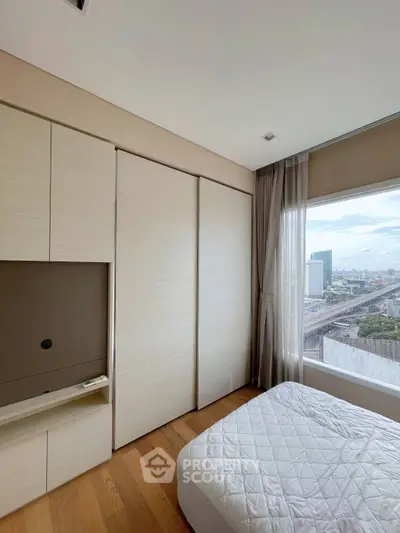Modern bedroom with large window offering city view and built-in wardrobe