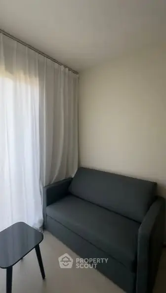 Cozy corner with a sleek gray sofa and sheer curtains, perfect for relaxation.