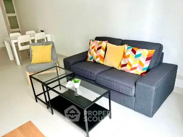 Modern living room with colorful cushions and sleek glass coffee table.