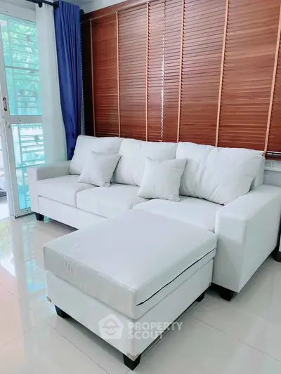 Modern living room with white sofa and ottoman, wooden blinds, and glass sliding door.