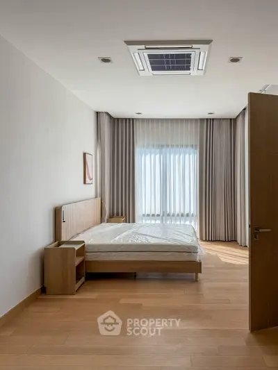 Modern bedroom with wooden flooring and large window with curtains.