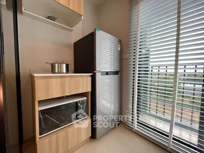 Modern kitchen with sleek fridge and microwave, featuring large window with blinds and outdoor view.