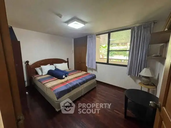 Cozy bedroom with large window and wooden flooring, perfect for relaxation.