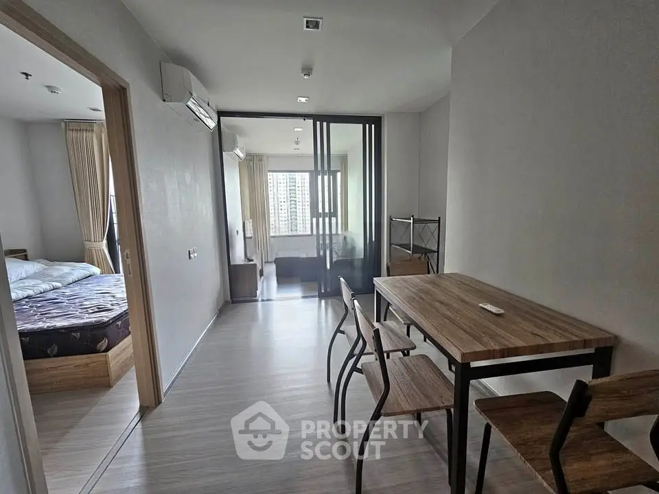 Modern apartment interior with dining area and bedroom view, featuring sleek wooden furniture and large windows.