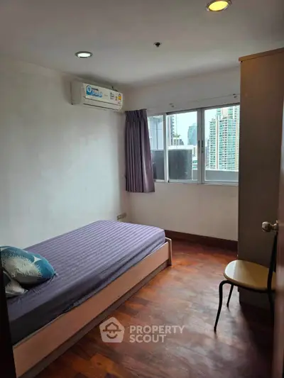 Cozy bedroom with city view, featuring wooden flooring and air conditioning, perfect for urban living.