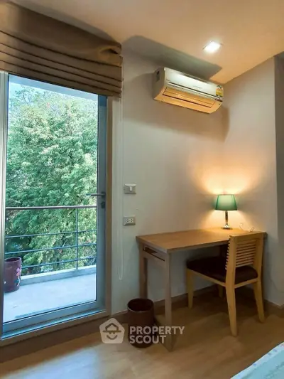 Cozy study nook with desk and chair next to a balcony with lush green view, perfect for work-from-home setup.