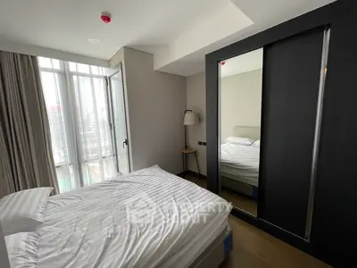 Modern bedroom with large window and mirrored wardrobe in urban apartment.