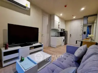 Modern living room with cozy sofa, flat-screen TV, and compact kitchen in open layout apartment.