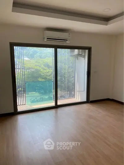 Spacious room with large window and balcony overlooking lush greenery, perfect for serene living.