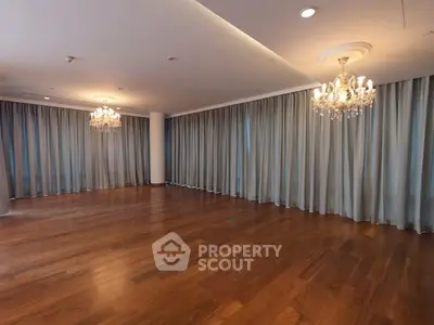 Spacious empty room with elegant chandeliers and wooden flooring, perfect for luxurious living.