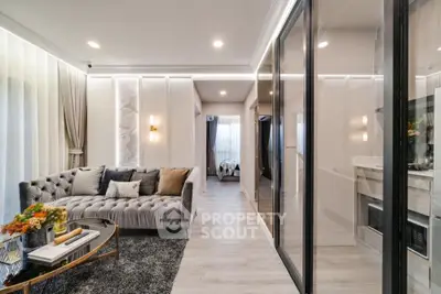 Elegant living room with plush grey sofa, chic decor, and modern kitchen visible through glass partition, perfect for upscale urban living.
