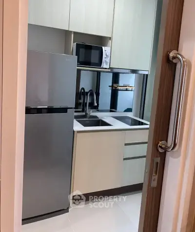 Modern compact kitchen with stainless steel fridge and microwave, sleek cabinetry, and dual sink.