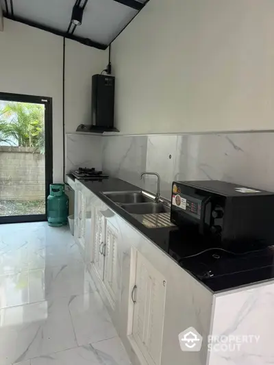 Modern kitchen with sleek marble countertops and gas stove, featuring a microwave and ample natural light.