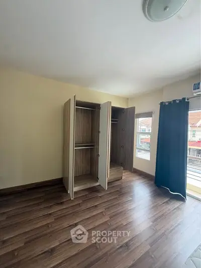 Spacious bedroom with wooden flooring and open wardrobes, featuring large windows for natural light.