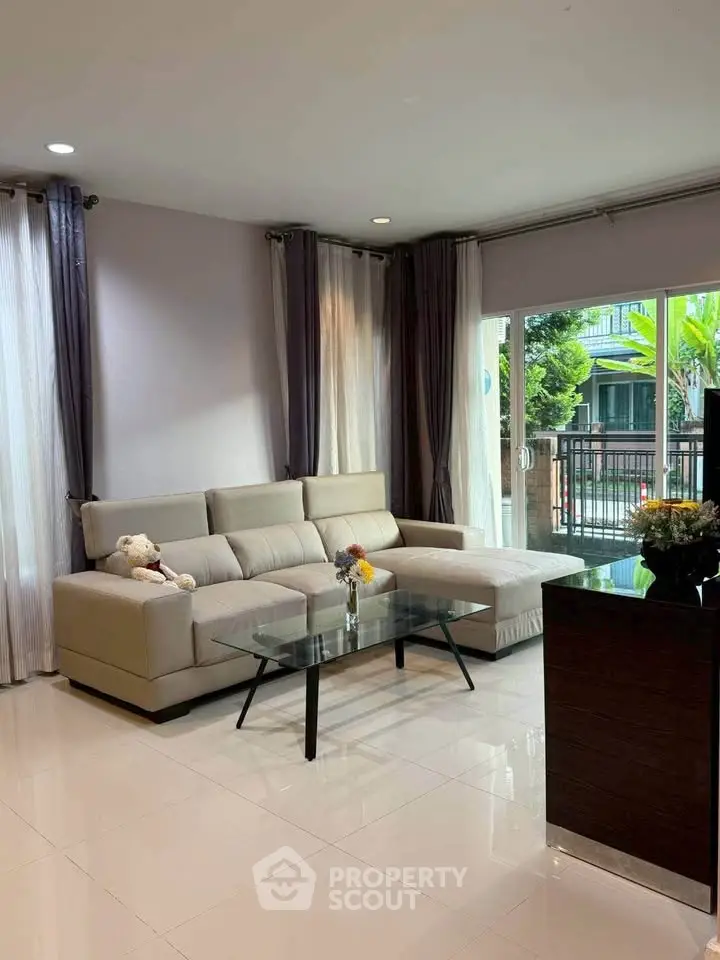 Spacious living room with modern sofa and glass coffee table, large windows with garden view.