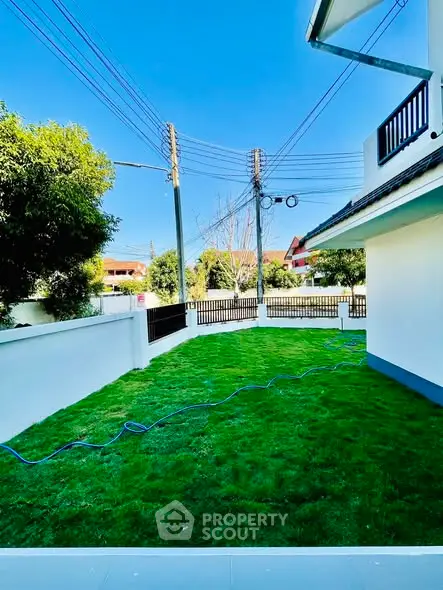 Spacious green garden area with modern house exterior and clear blue sky.